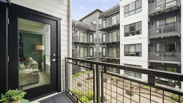 A modern apartment building with multiple balconies, a glass door entrance, and a small outdoor seating area.