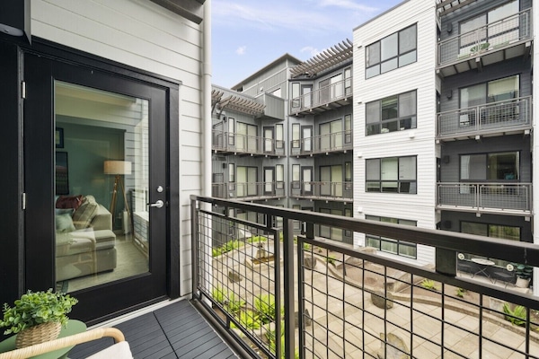 Quiet outdoor balcony area with modern railing, seating space, and views of the surrounding courtyard and neighboring buildings, offering a peaceful urban retreat.