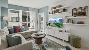 Una sala de estar moderna con sofá, mesa de centro, televisor, estanterías y vistas a un edificio.