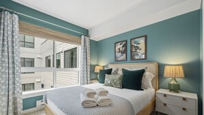 Un dormitorio con una cama grande, dos mesitas de noche, una ventana con cortinas y una obra de arte en la pared.