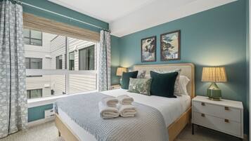 A bedroom with a large bed, two bedside tables, a window with curtains, and artwork on the wall.