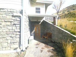 A stone exterior wall, a wooden door, a bench, and a grassy hillside. - A private apartment on six acres, with a view no other listing in Gardiner has. (Gardiner)