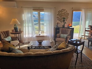 A living room with a sofa, armchairs, a coffee table, and a view of mountains through large windows. - A private apartment on six acres, with a view no other listing in Gardiner has. (Gardiner)