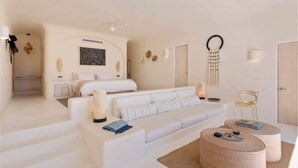 Una habitación de hotel moderna con un sofá blanco, una mesa de centro redonda y una cama con cabecera.