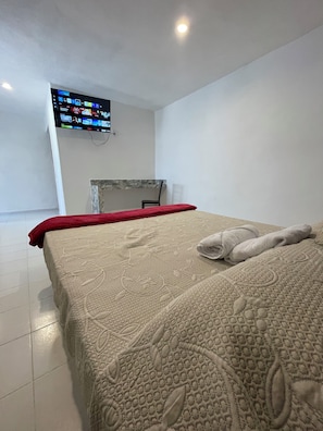 Una habitación de hotel con cama, televisión montada en la pared y escritorio con silla.