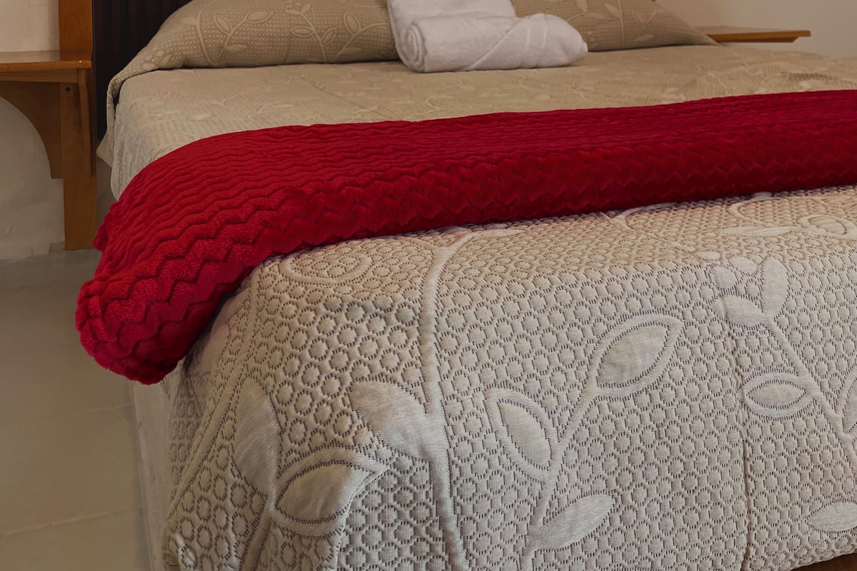 Una cama con cabecera de madera, una manta roja y una colcha estampada.