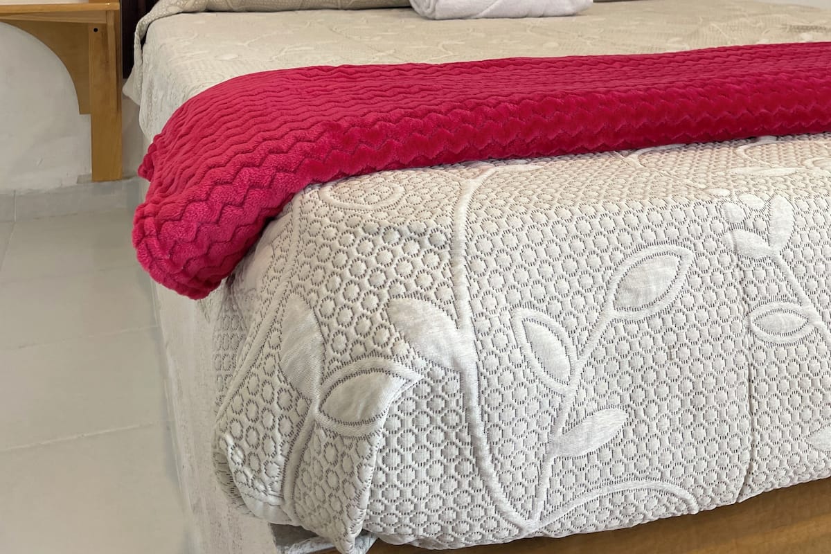 A bed with a wooden headboard, a white and red blanket, and a patterned bedspread.