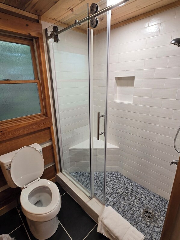 A bathroom with a toilet, a glass-enclosed shower, and a tiled floor.