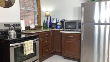 A kitchen with an oven, microwave, refrigerator, and a kettle on the stove.