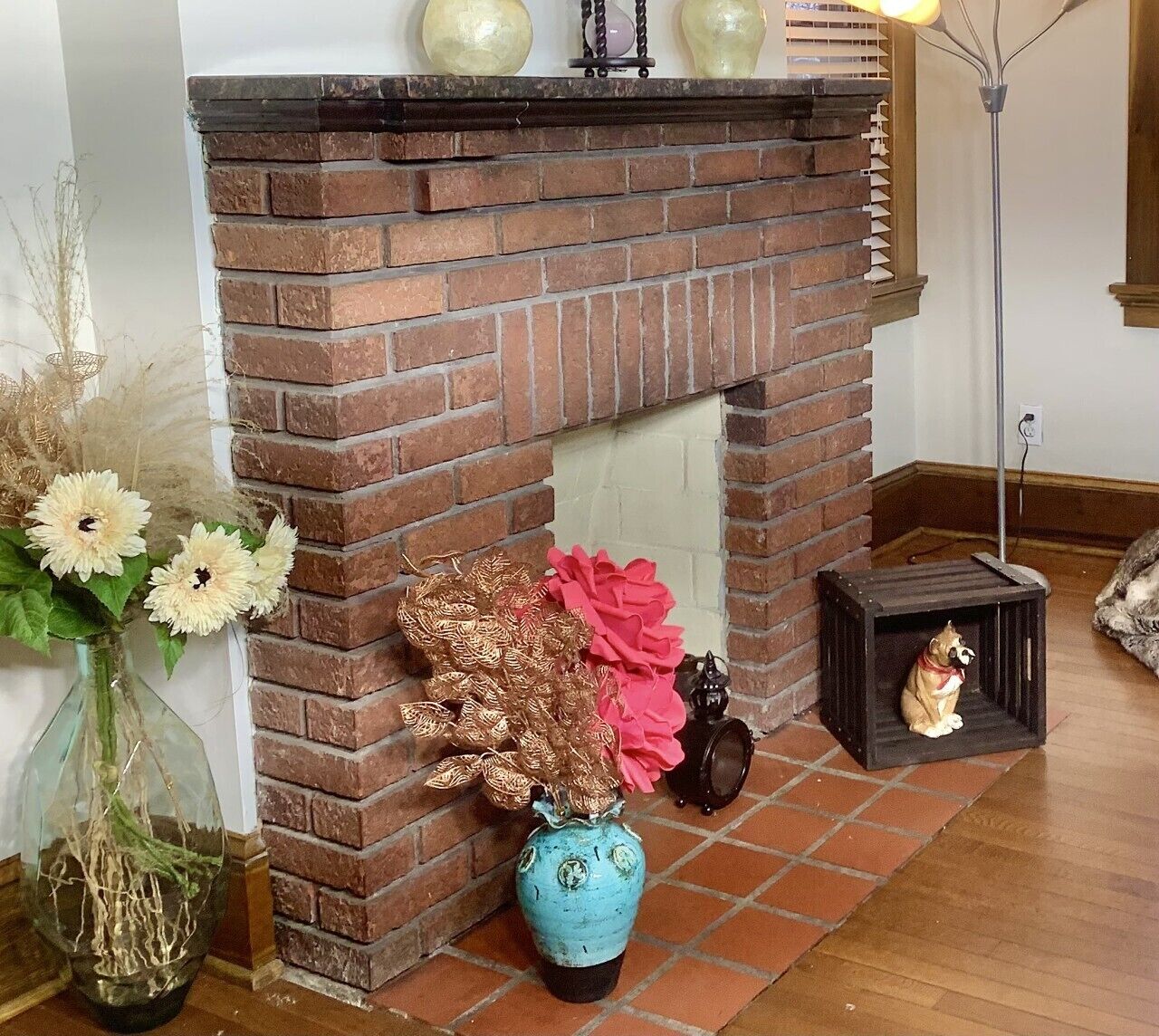 A brick fireplace with decorative items, a vase with dried plants, and a small dog crate.