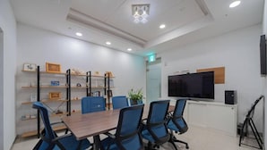 A conference room with a long table, blue chairs, shelves with framed items, a TV, and a plant. - Cordelia Hotel Geoje (Geoje)