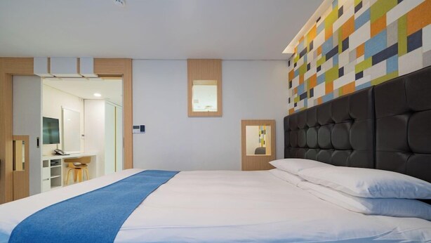A modern hotel room with a large bed, a desk, and a bathroom visible through an open door. - Cordelia Hotel Geoje (Geoje)