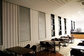 Un intérieur de restaurant moderne, avec de hauts plafonds, des stores verticaux et un long comptoir doté de sièges.