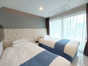 A hotel room with two beds, a large window with curtains, and a ceiling light. - Cordelia Hotel Geoje (Geoje)