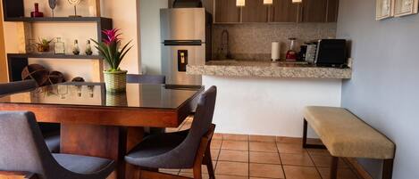 A modern kitchen with a dining table, chairs, a bench, and a refrigerator.