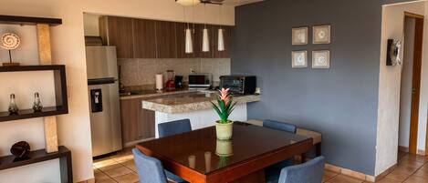 A modern kitchen with a dining area, featuring a wooden table, blue chairs, and a ceiling fan.