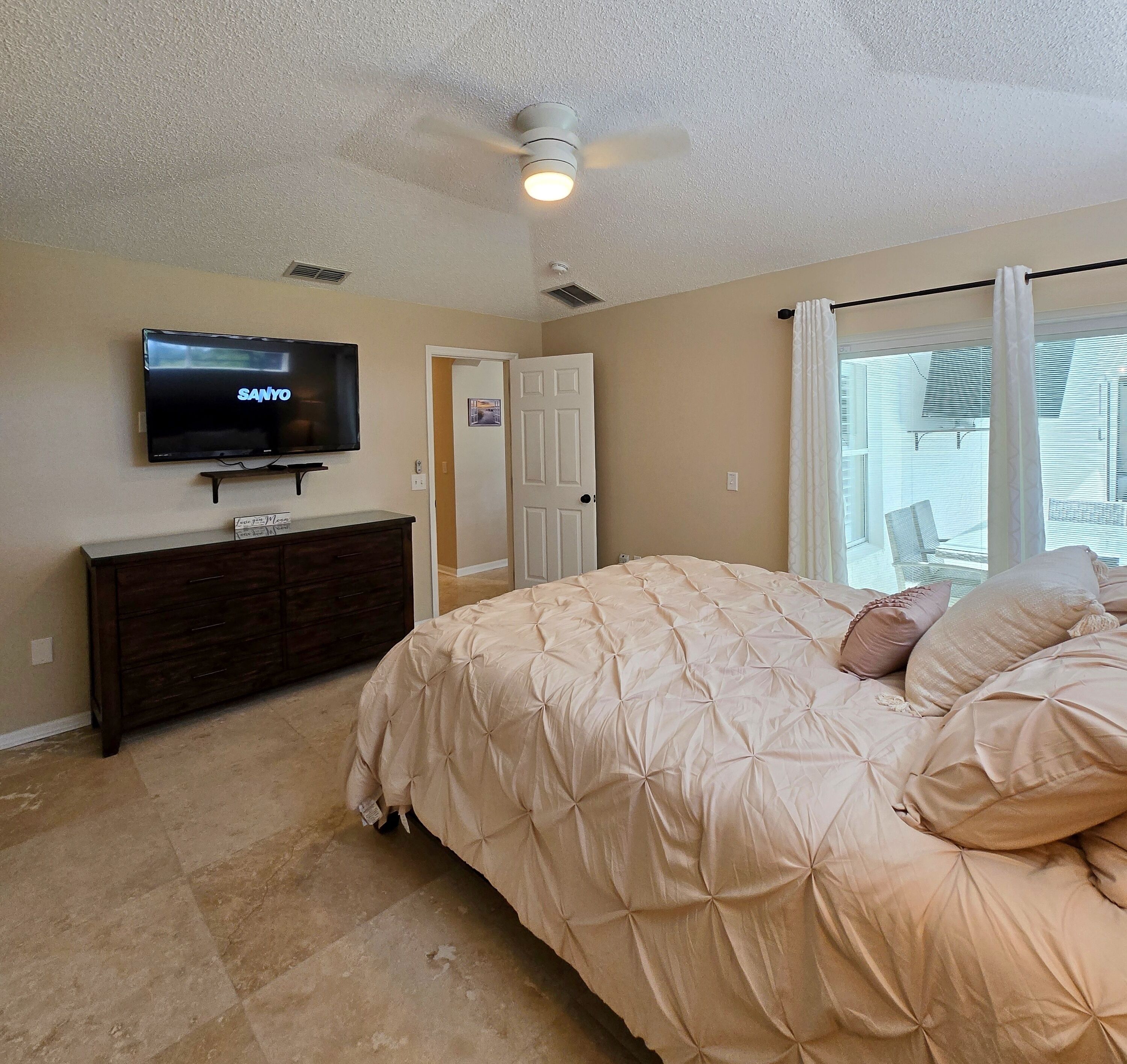 A bedroom with a bed, a TV, a ceiling fan, and a window with curtains.