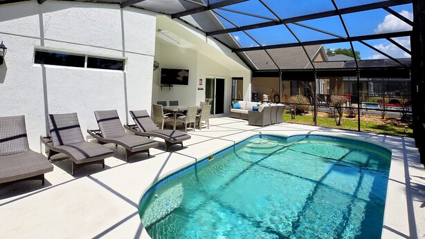 A swimming pool with lounge chairs, a covered patio, and a view of the surrounding area. - 4BR 3Bath Pool Home with Golf Course View, Quiet Cul De sac in Southern Dunes (Haines City)
