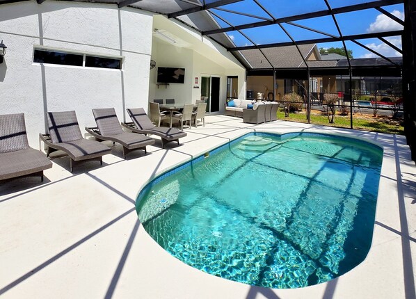 A swimming pool with lounge chairs, a covered patio, and a view of the surrounding area. - 4BR 3Bath Pool Home with Golf Course View, Quiet Cul De sac in Southern Dunes (Haines City)