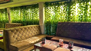 A seating area with cushioned sofas and ottomans, a marble-patterned floor, and a wall covered with green foliage. - Rosepearl Hotel And Suites (Lagos)