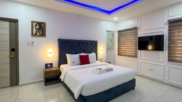 A modern bedroom with a large bed, bedside lamps, a flat-screen TV, and a ceiling light fixture. - Rosepearl Hotel And Suites (Lagos)