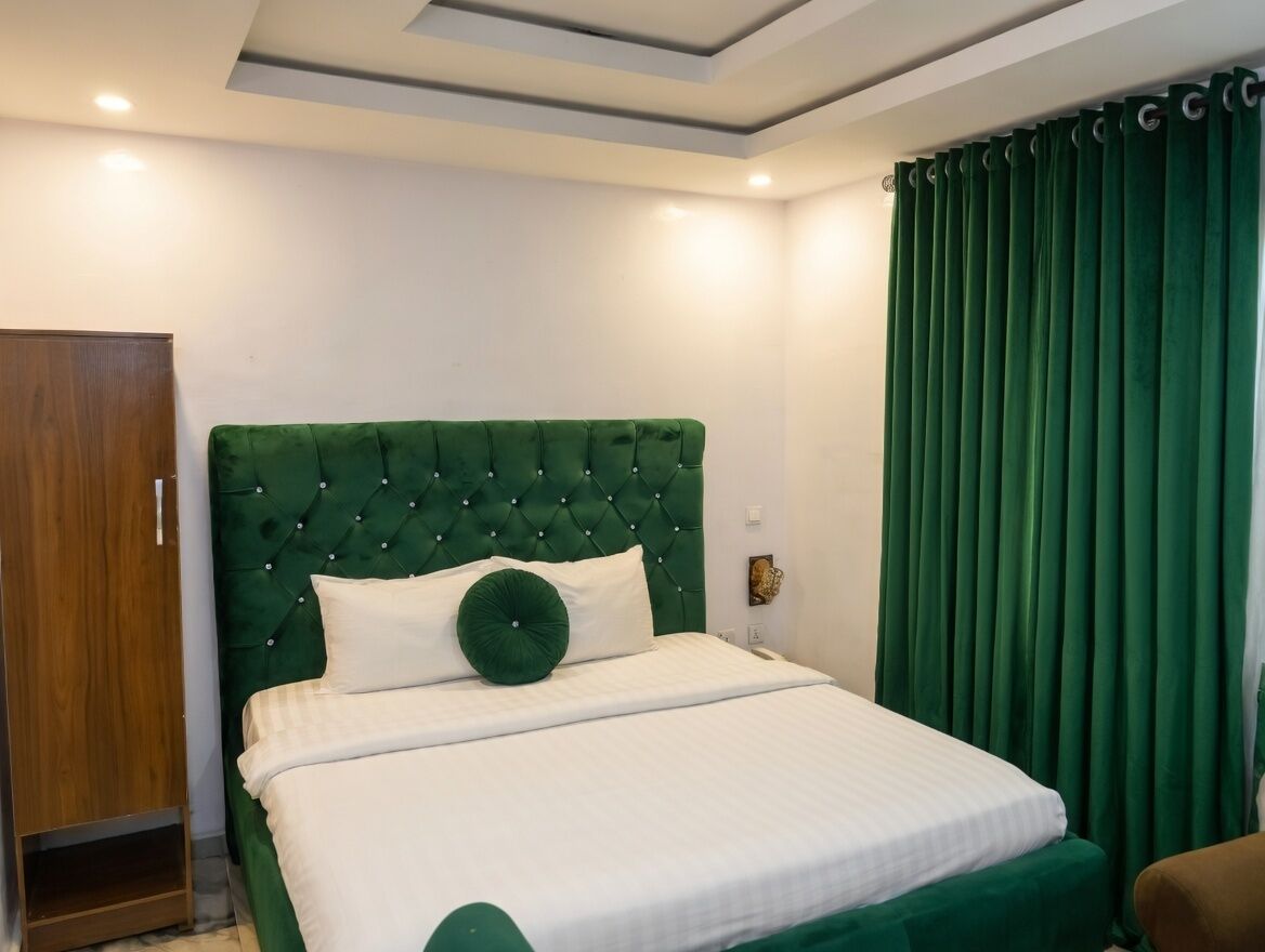 A neatly made bed with a tufted headboard, a wooden wardrobe, and a green curtain.