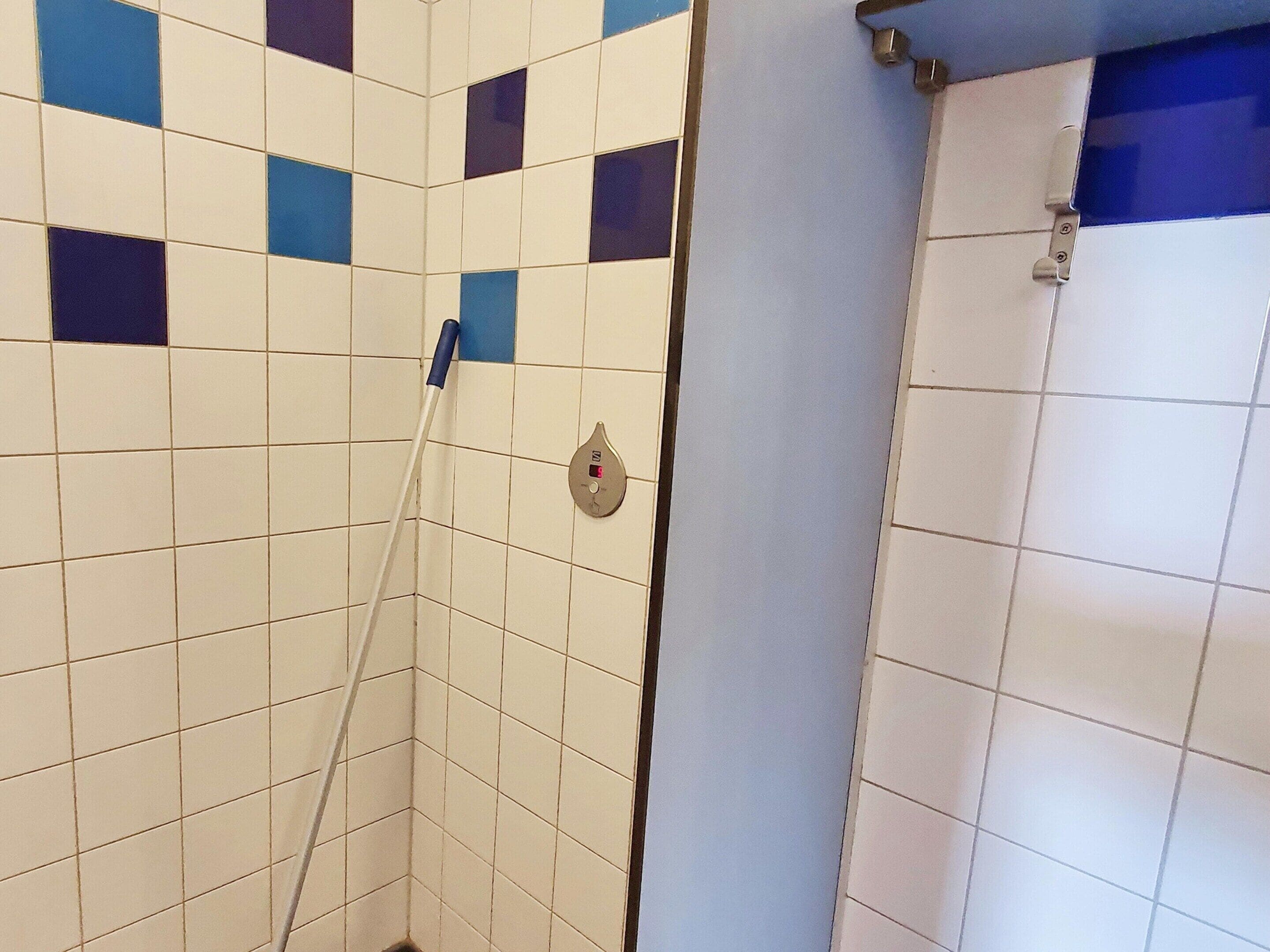A corner of a bathroom with white and blue tiles, a shower curtain, and a showerhead.