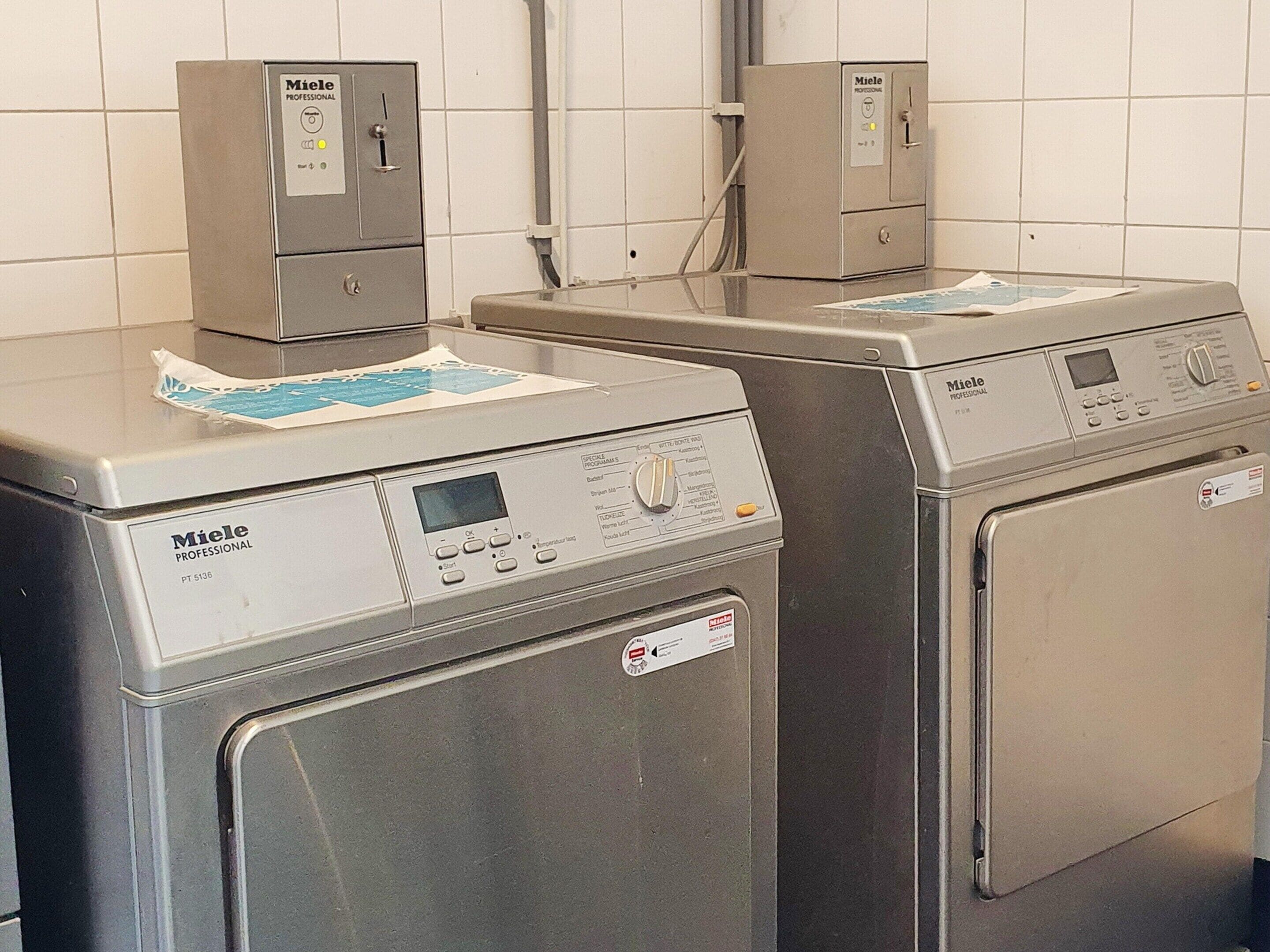 Two professional-grade Miele washing machines in a tiled room.