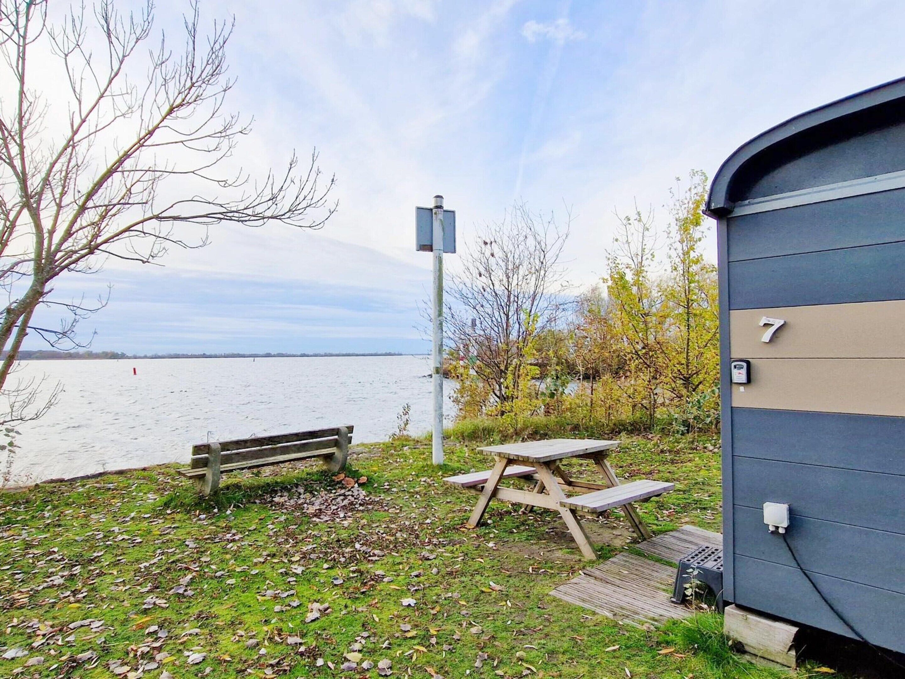 Un entorno junto al lago con una mesa de picnic, un banco y un edificio con el número 7.