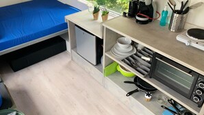 Habitación compacta con cama, kitchenette y ventana con vistas a zonas verdes.