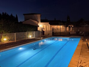 A swimming pool with a tiled deck, a white fence, and a building with a lighted entrance. - Villa with pool (Saint-Jean-de-Cuculles)