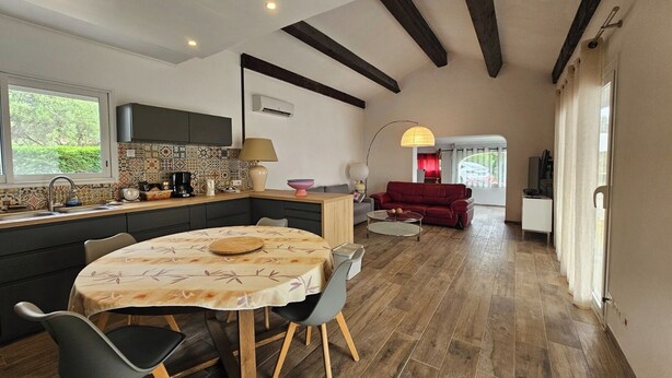 Een moderne keuken met een eethoek, houten vloeren en een rode bank in de woonkamer.