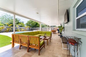 Eine Terrasse im Freien mit einer Holzbank, einem grünen Sofa und einem an der Wand befestigten Fernseher.