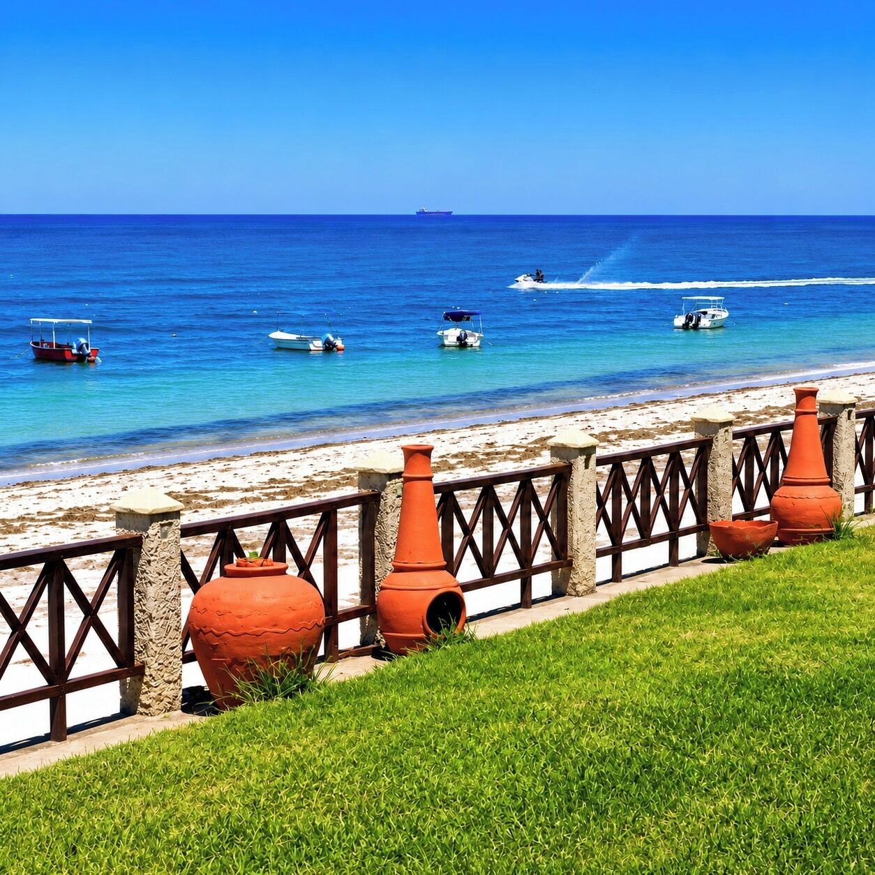 A beach with a fence, potted plants, and a clear blue sea.