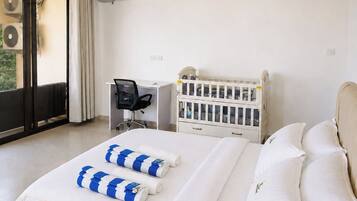 A hotel room with a bed, a desk, a chair, a crib, and an air conditioning unit.