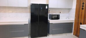 A kitchen with a black refrigerator, a microwave, and grey cabinets.