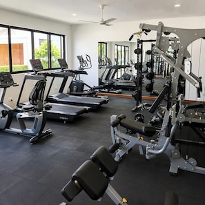 Une salle de sport équipée de tapis de course, d’appareils de musculation et d’un ventilateur de plafond.