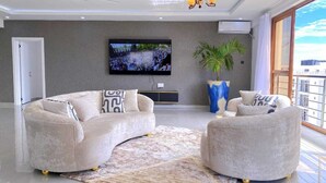 Ein modernes Wohnzimmer mit einer gebogenen Couch, einem Fernseher, einem großen Fenster und einer Pflanze.