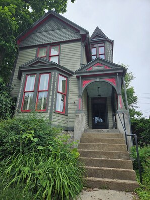 Une maison à deux étages avec un porche, une porte d’entrée et un escalier menant à l’entrée.