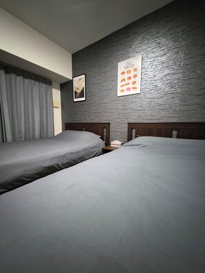A bedroom with two single beds, a nightstand, a framed picture, and a wall-mounted poster. - HK House (Osaka)