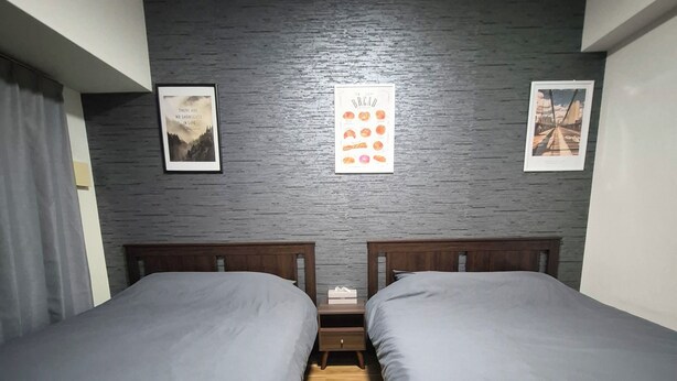Ein Zimmer mit zwei Betten, Holzboden, einer strukturierten grauen Wand und gerahmten Bildern.
