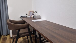 Ein Konferenzraum mit einem langen Holztisch, zwei braunen Stühlen, einer gerahmten Pflanze und einer Whiteboard-Tafel.