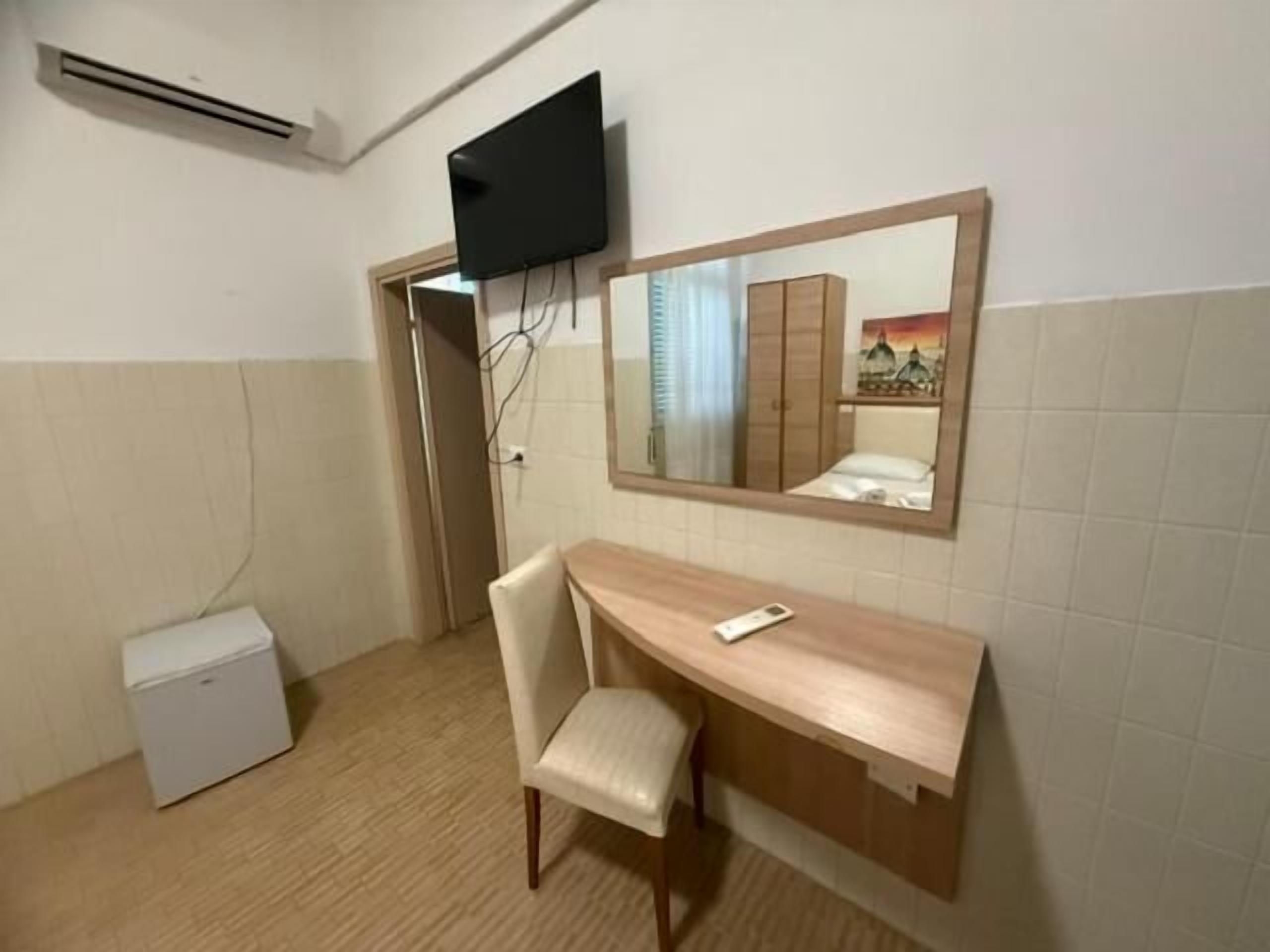 Ein kleines Zimmer mit Schreibtisch, Stuhl und einem an der Wand befestigten Fernseher.