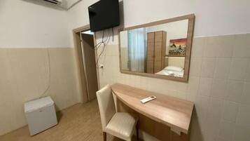 Ein kleines Zimmer mit Schreibtisch, Stuhl und einem an der Wand befestigten Fernseher.