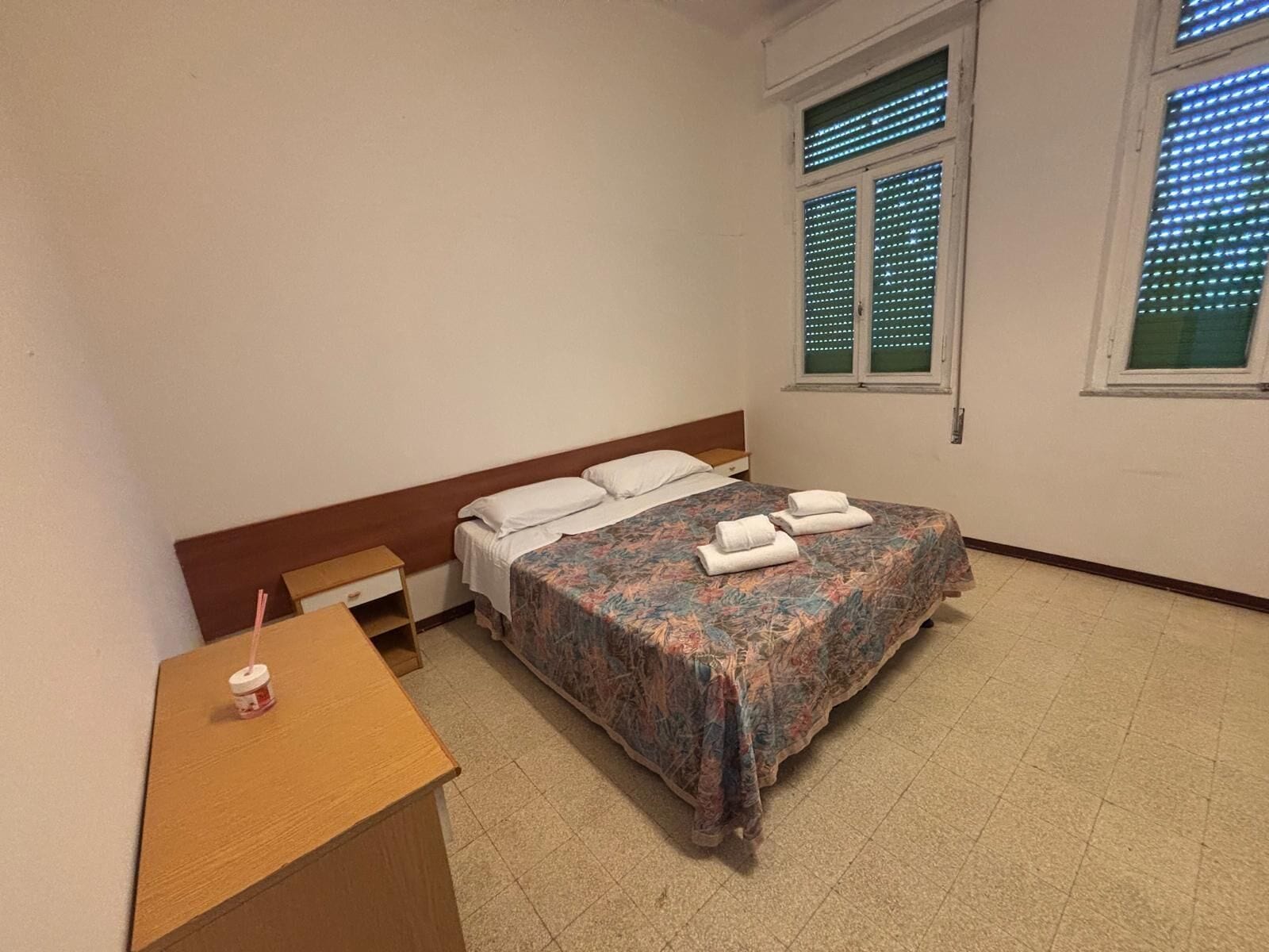 Une chambre à coucher avec un lit, une table de chevet, une fenêtre avec des stores et une petite table sur laquelle est posée une bougie.