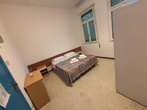 A bedroom with a bed, a desk, a window with blinds, and a door.
