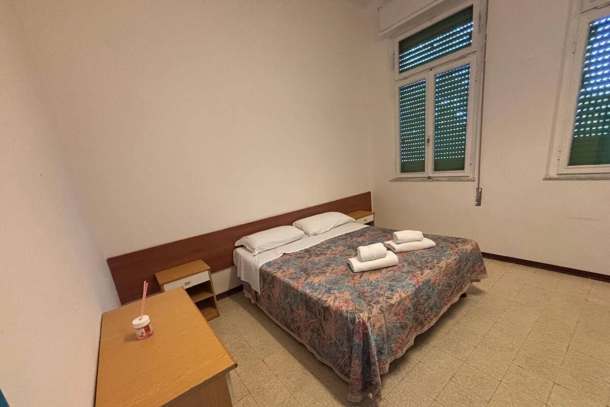 Ein Zimmer mit einem Bett, einem Holztisch und einem Fenster mit Jalousien.