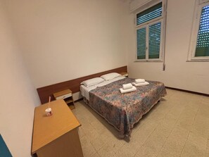 A room with a bed, a wooden desk, and a window with blinds.