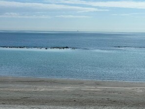 Una platja amb aigua tranquil·la, un horitzó llunyà i un cel serè.