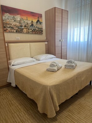 Habitación de hotel con cama, cabecero, armario, un cuadro y ventana con cortinas.
